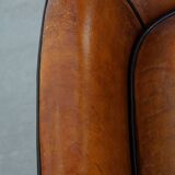 Cognac-colored sheepskin armchair with black piping and decorative nails