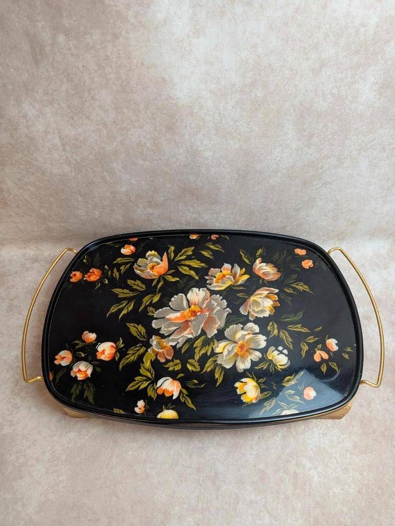 Large vintage 1960s platter with floral decoration on a black background and golden handles.