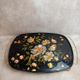 Large vintage 1960s platter with floral decoration on a black background and golden handles.