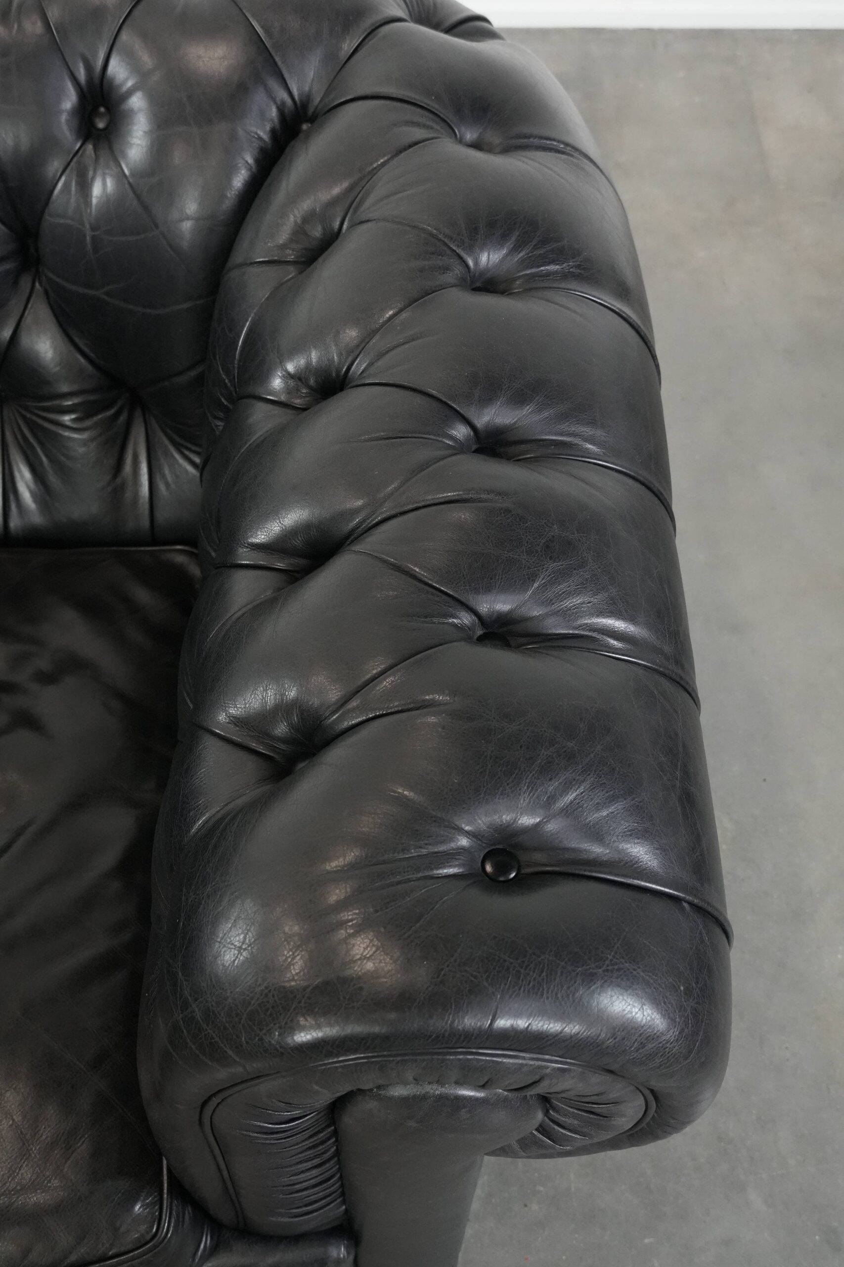 Ensemble composé d'un canapé chesterfield noir, d'un fauteuil et d'un pouf.