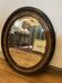 Vintage oval mirror adorned with a carved wooden frame; bronze/gold in patina.