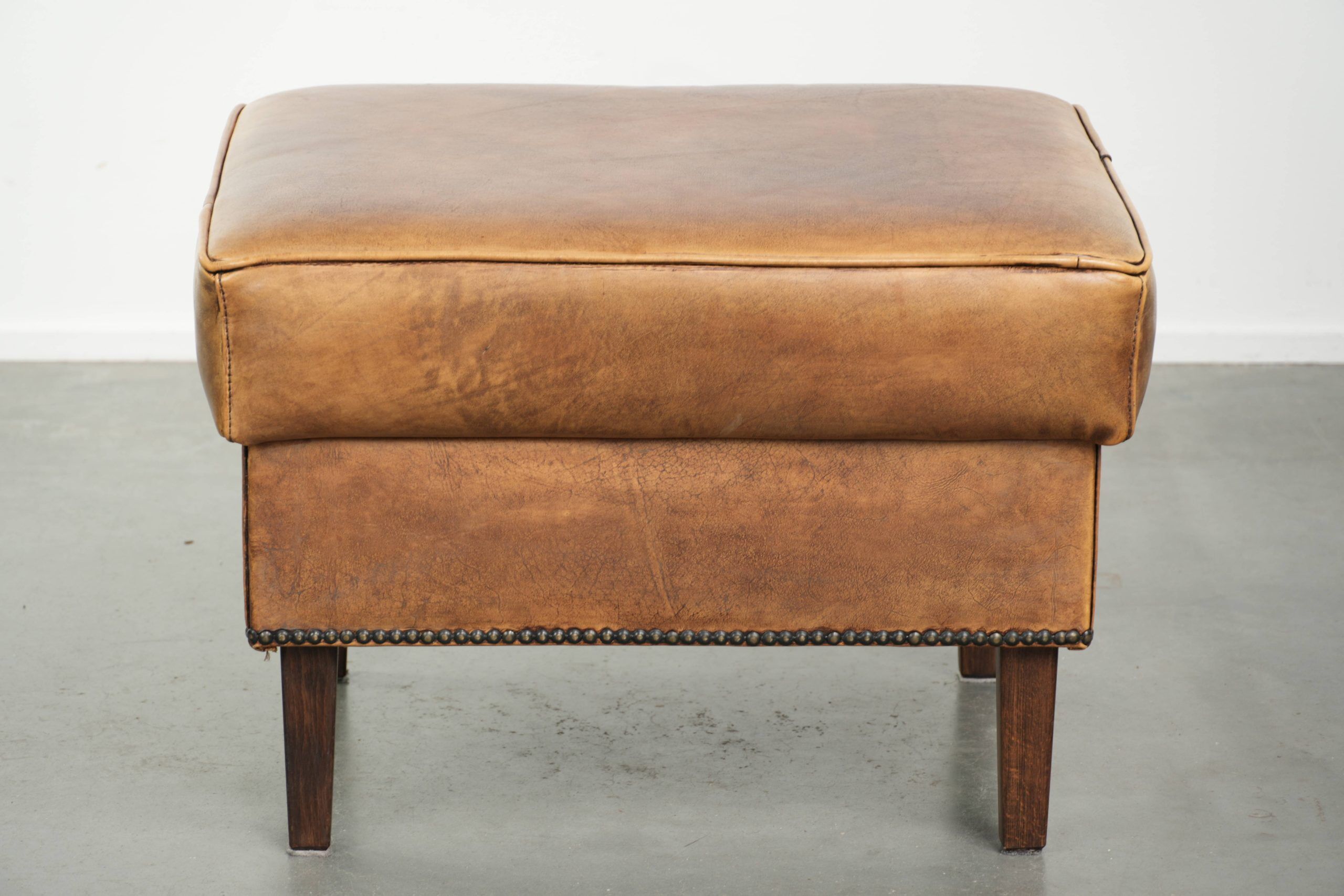 Cowhide ottoman with a beautiful patina finished with decorative nails