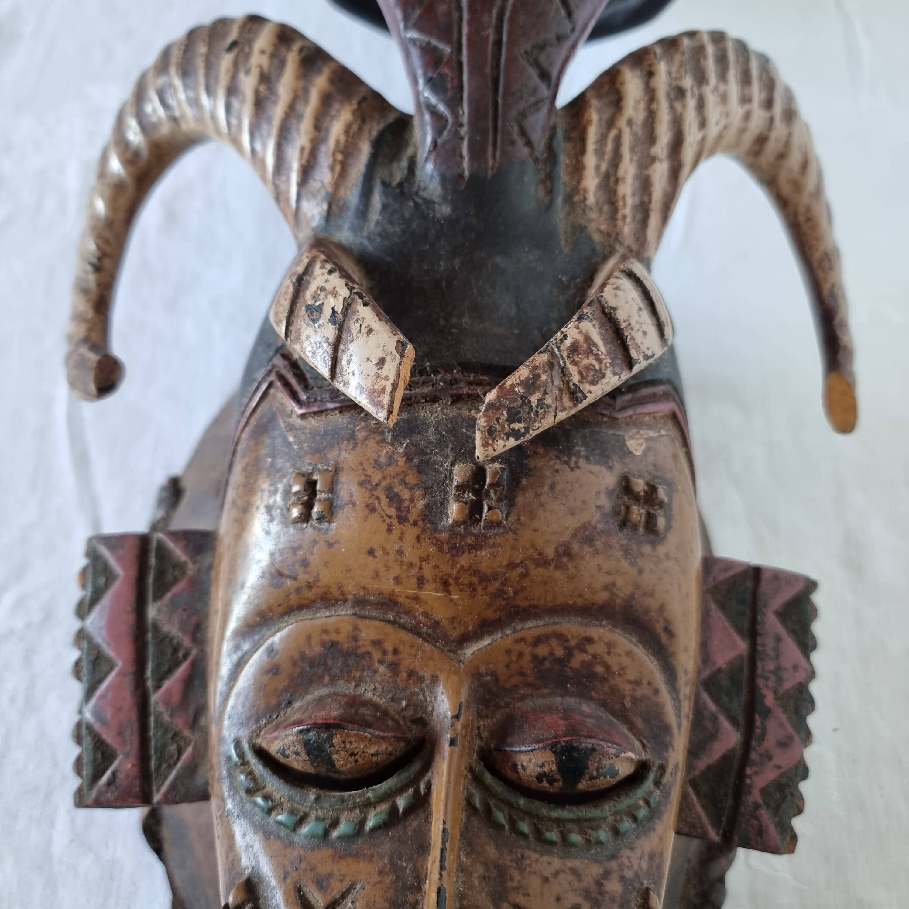 A large Senufo mask made of colored wood, decorated with an anthropomorphic figure