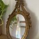 Oval convex witch mirror with golden ribbon mouldings.