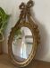 Oval convex witch mirror with golden ribbon mouldings.
