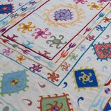 White suzani kilim rug with multi-colored embroidered patterns