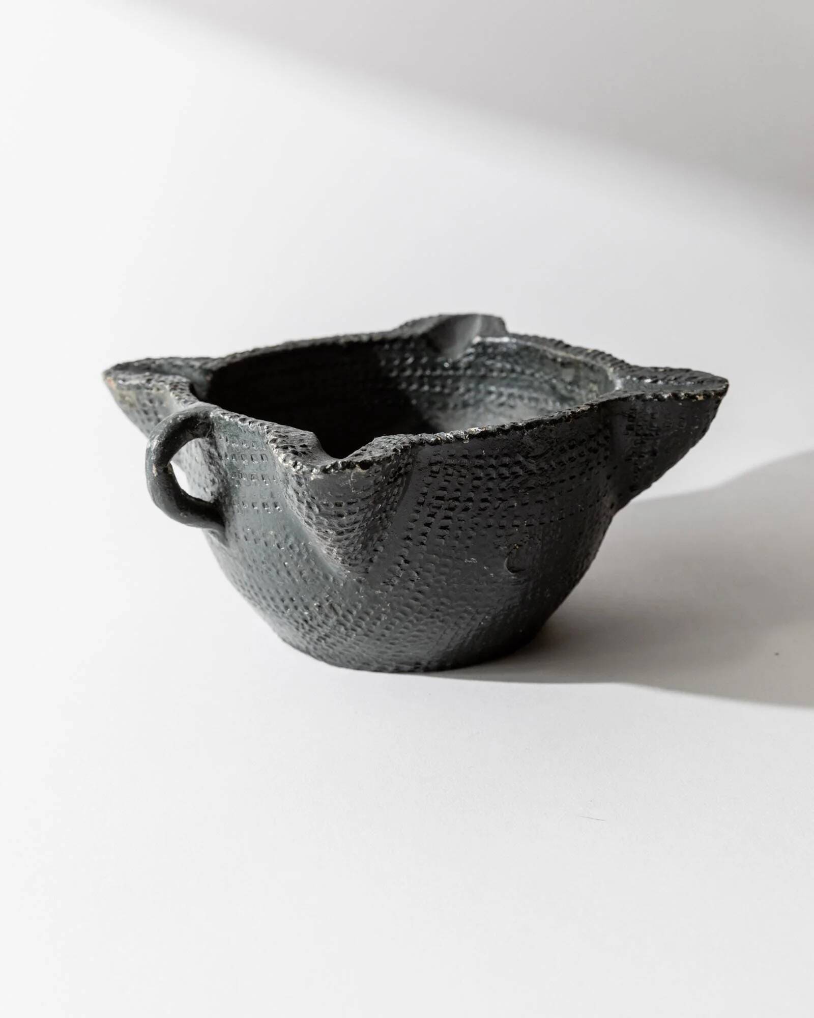 Vintage ceramic ashtray from the 1960s, black, hand-sculpted texture, organic shape.