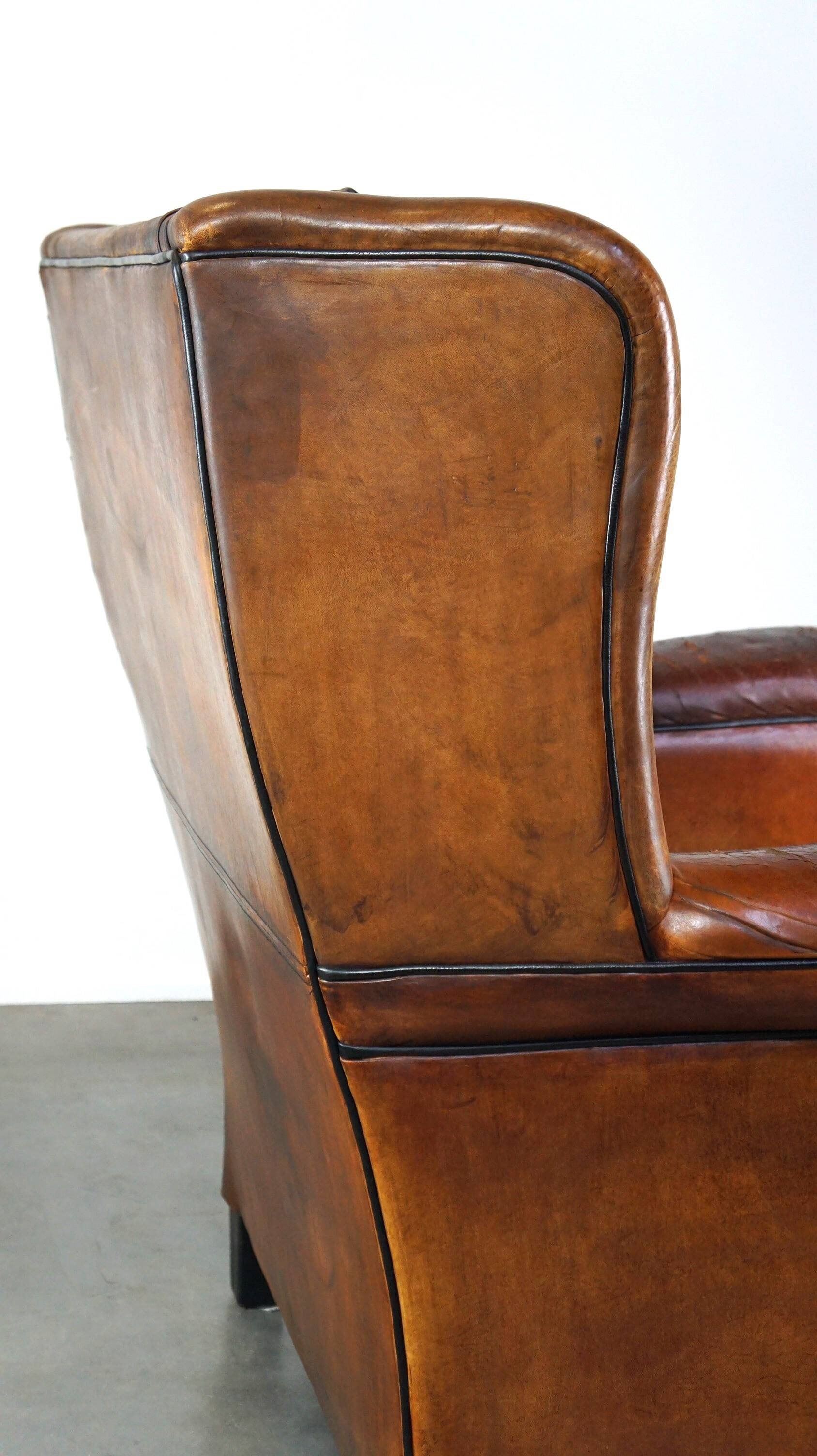 Very large worn sheepskin wing chair with a checked seat cushion