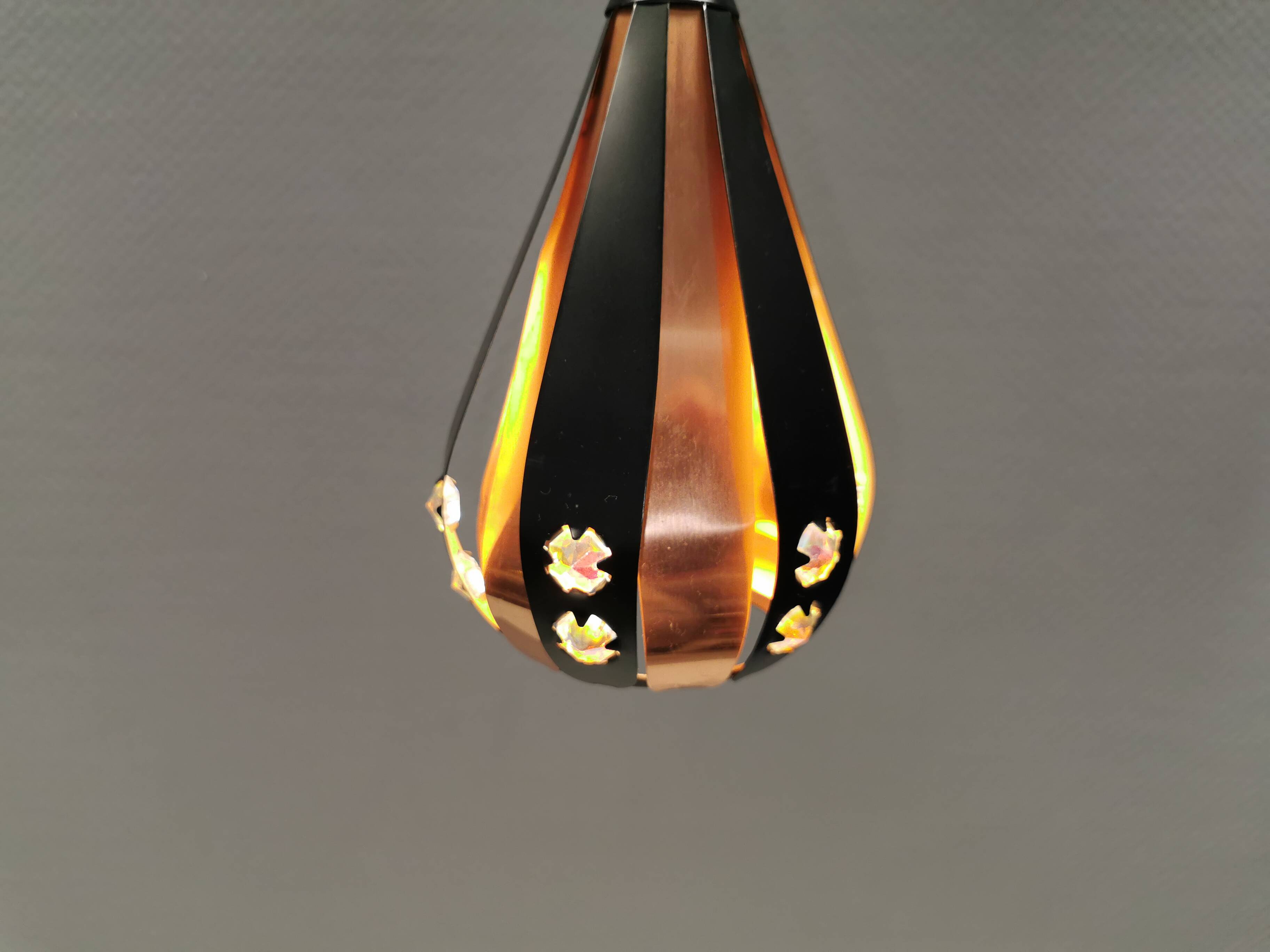 A teardrop-shaped pendant lamp made of copper, black metal, and prisms.