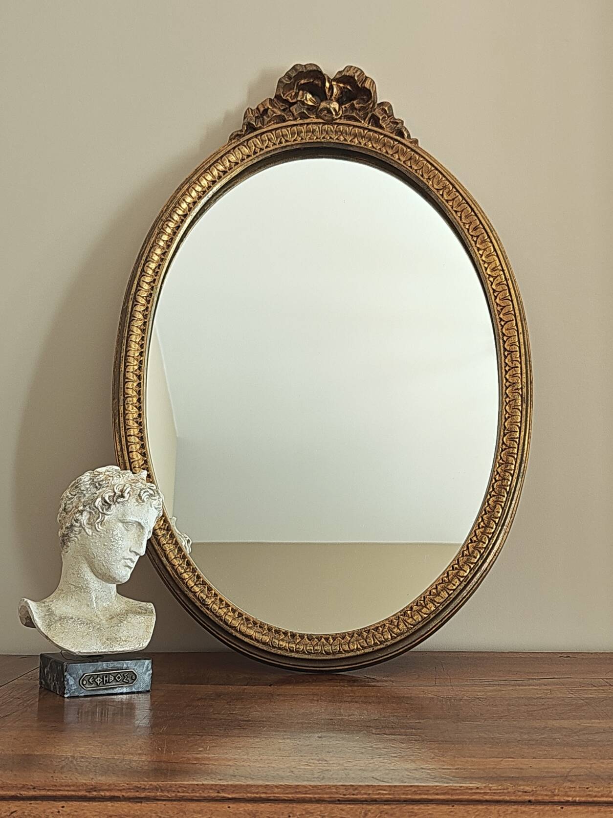 Vintage oval mirror with a carved wooden frame in gold, decorated with a bow.