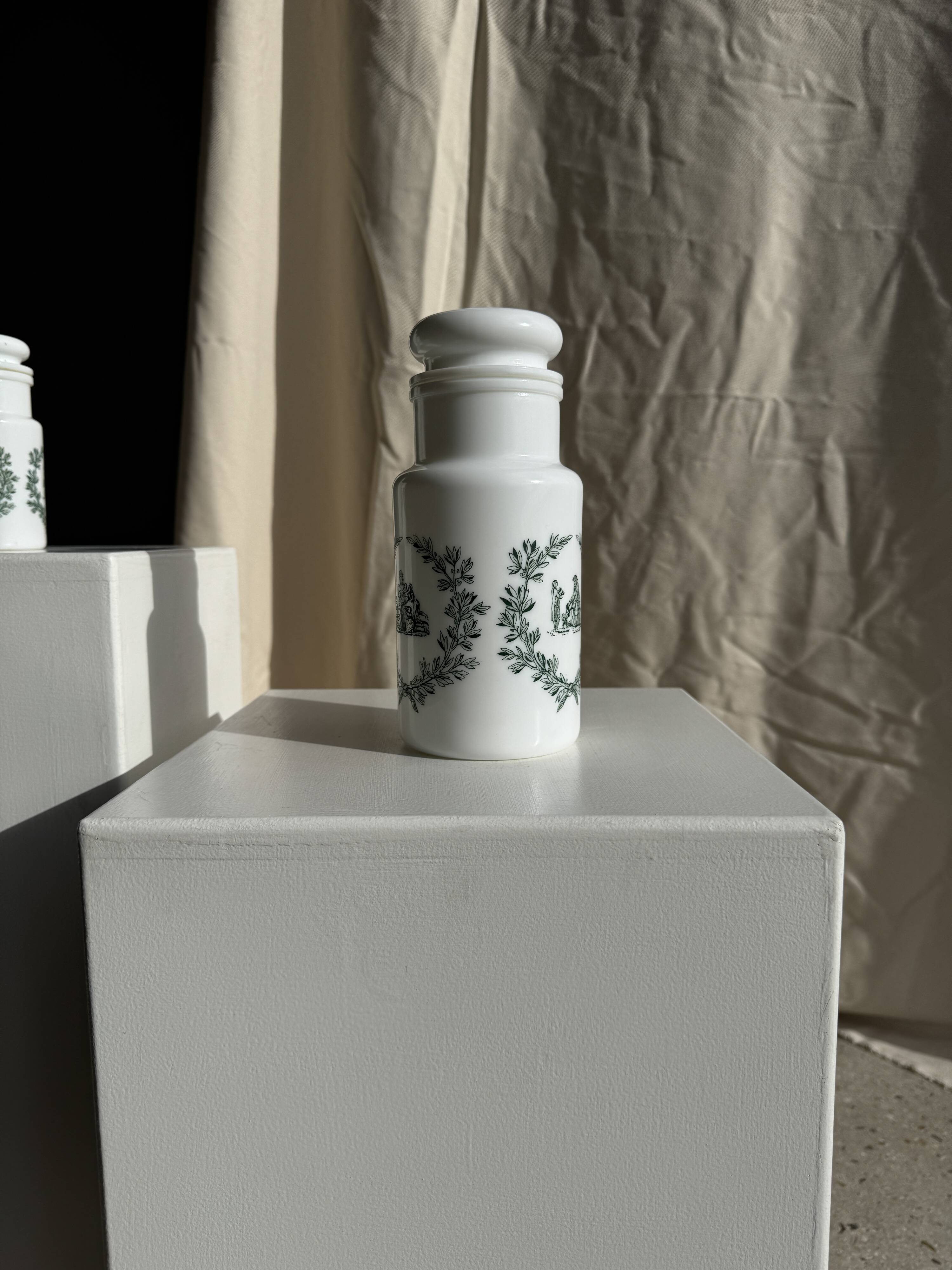 A pair of white glass bottles with Italian green patterns.