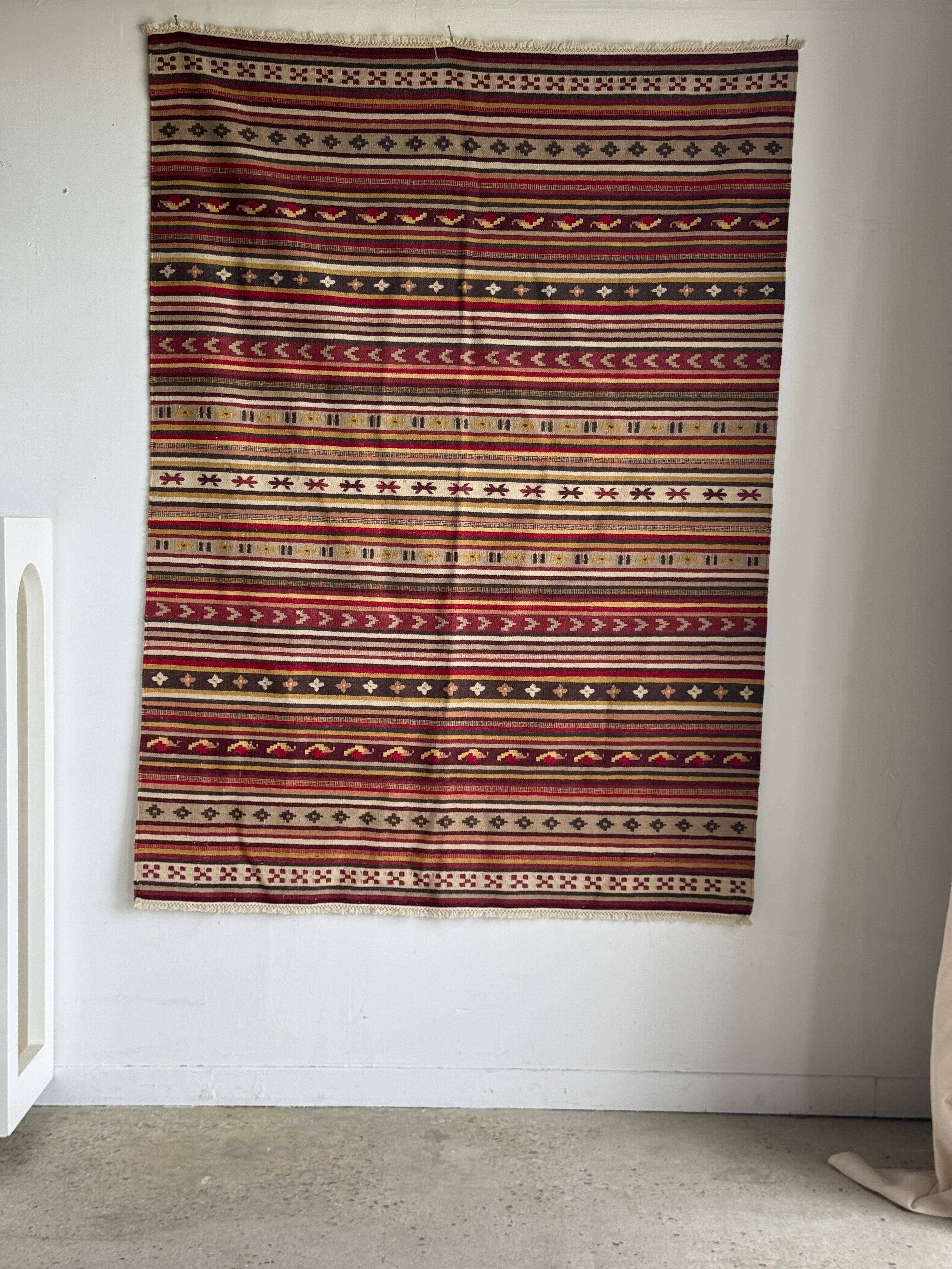 Large Indian rug with red, yellow, and white stripes and geometric fringes.