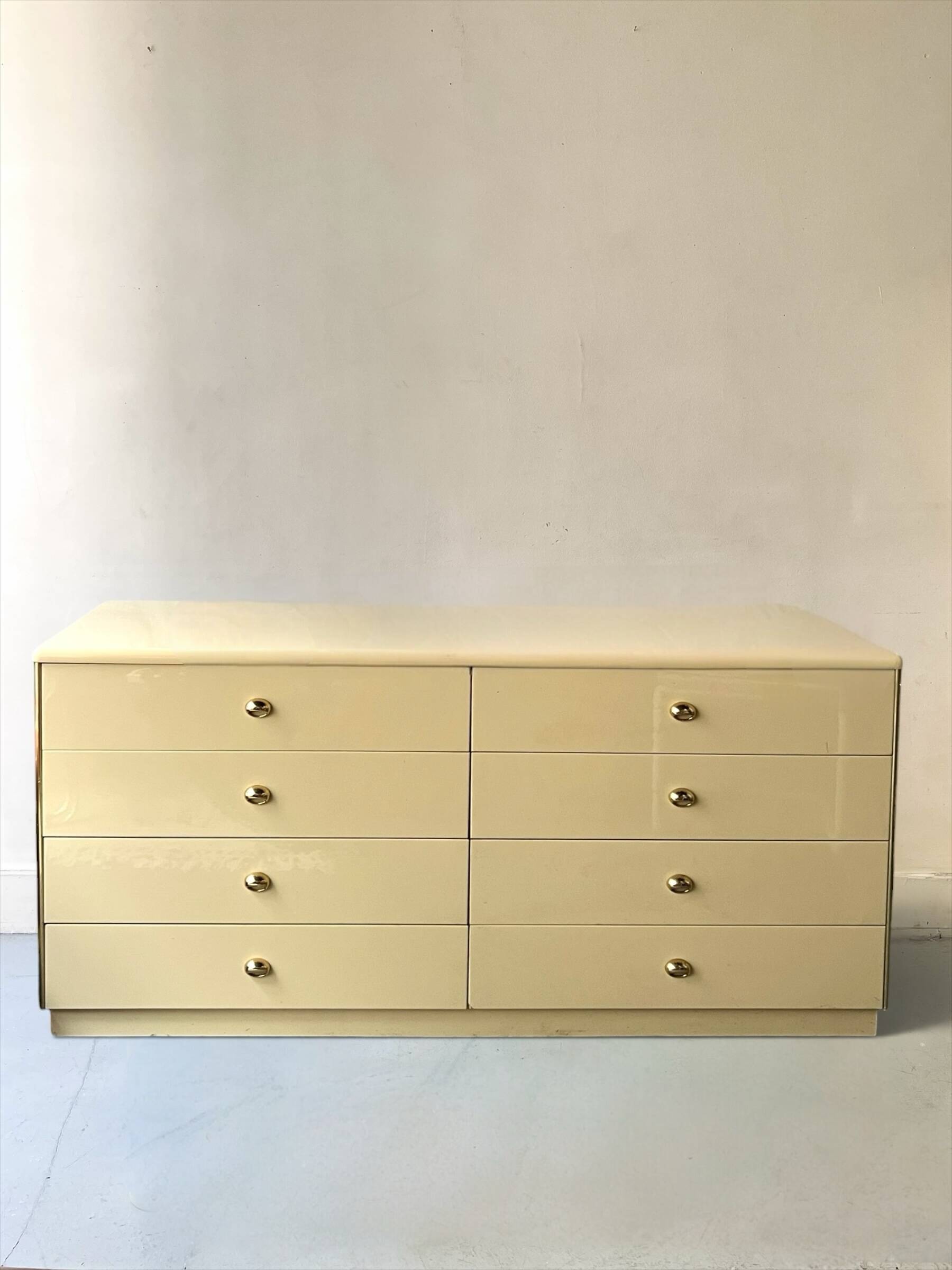 Commode type sideboard with 8 drawers, ivory lacquer and brass details, 1970s design.