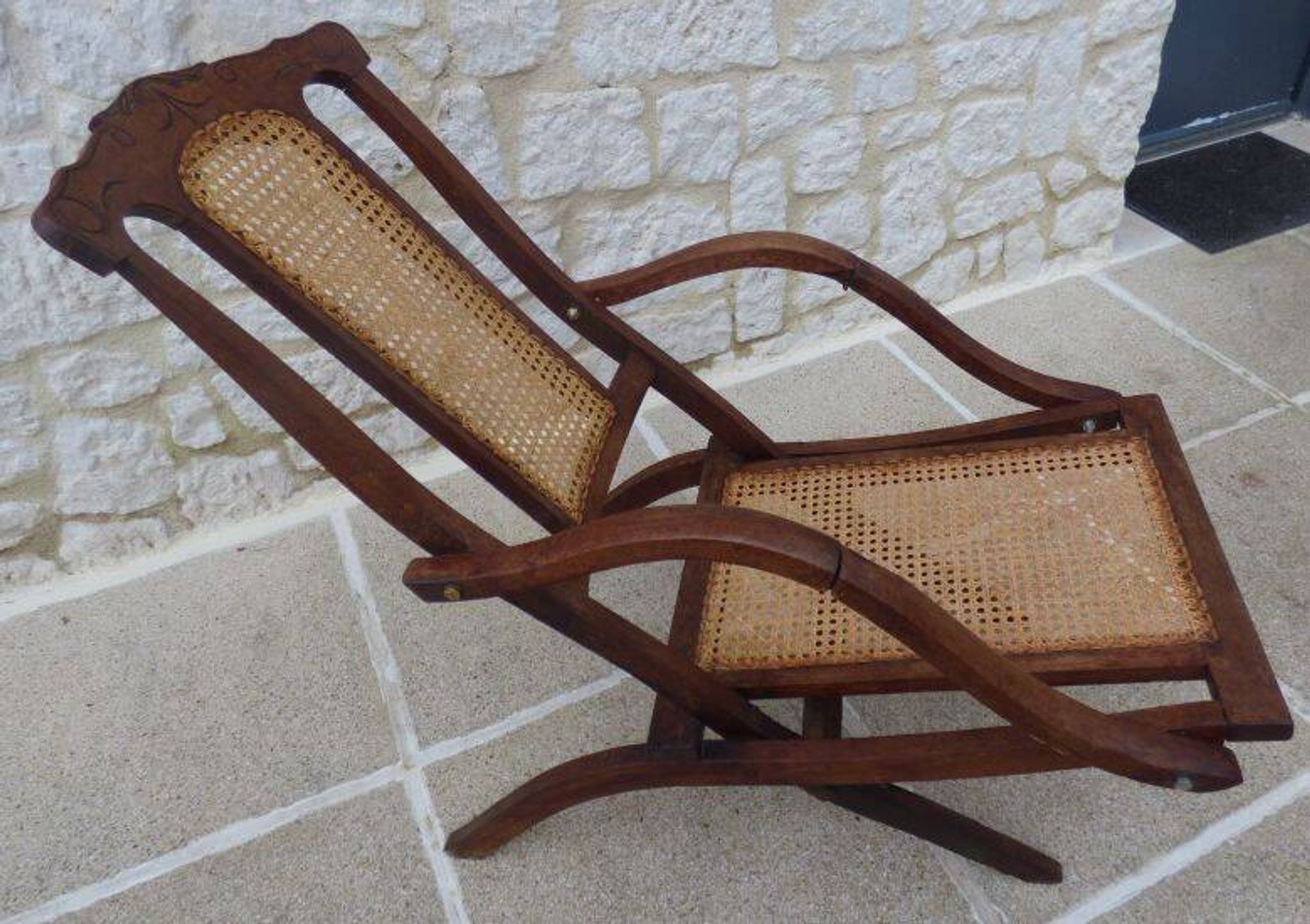Antique folding chair with caned seat and backrest made of wood.
