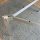 Round dining table with a glass top and brushed metal triangular frame.