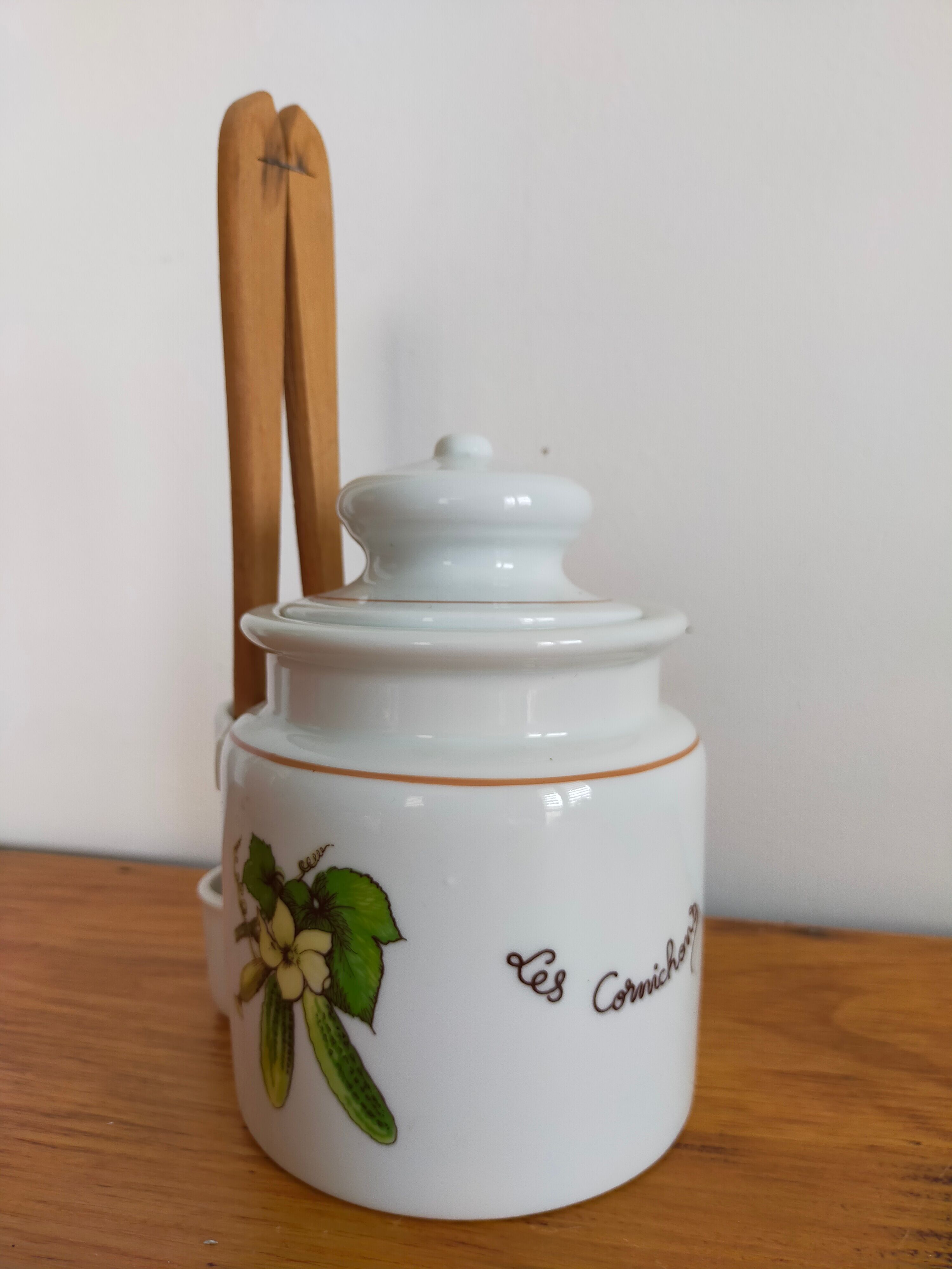 Vintage porcelain pickle pot with wooden pliers.
