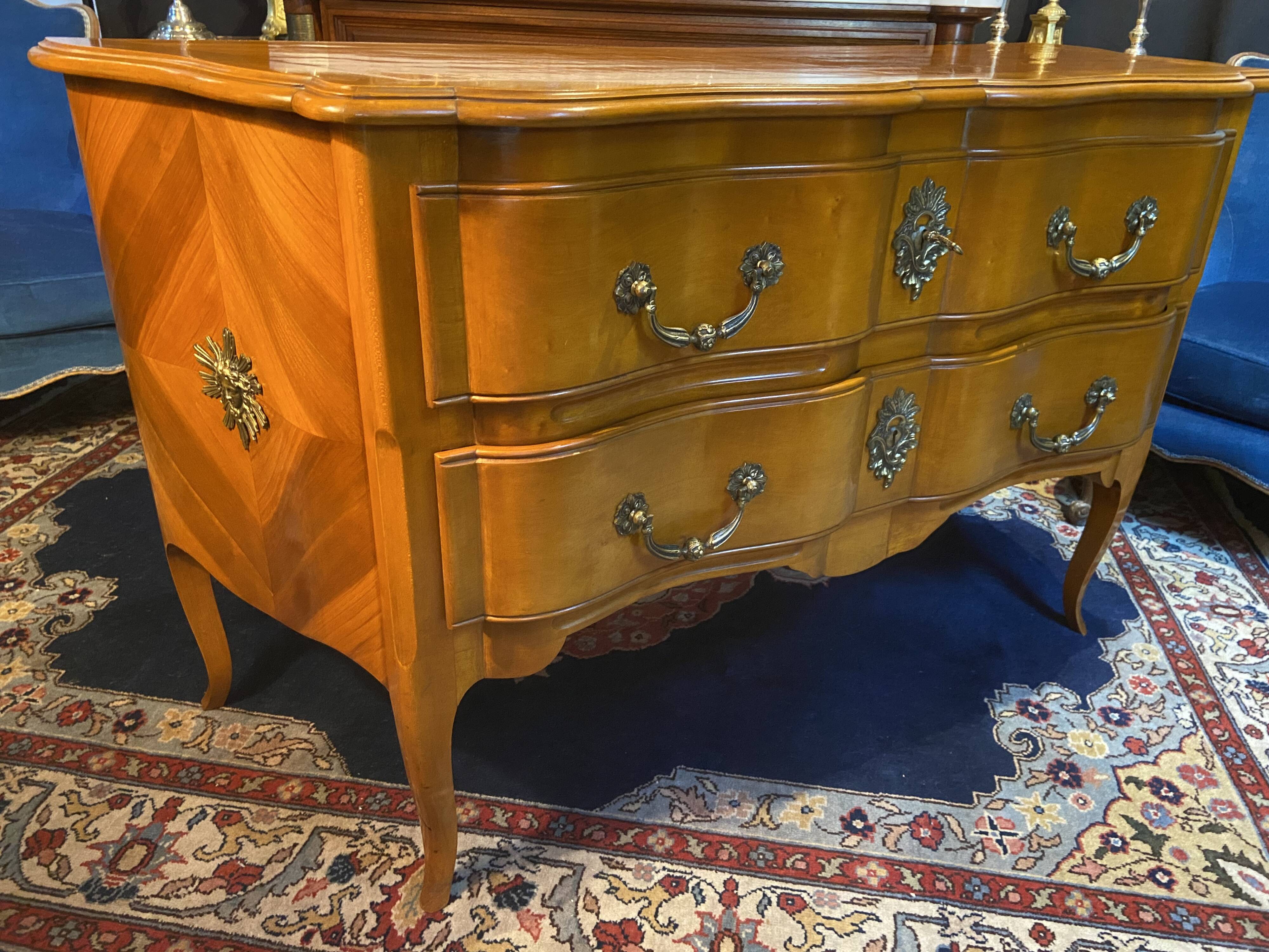 Large bow-fronted chest of drawers in blonde cherry with bronze ornamentation.