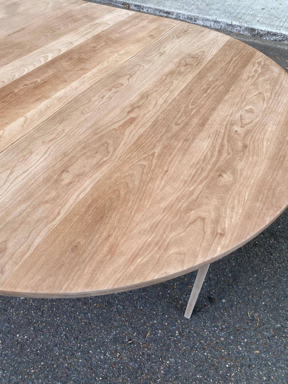 Large extendable round dining table stripped in solid cherry wood with a central leg.
