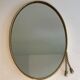 Oval brass mirror surrounded by a cord.