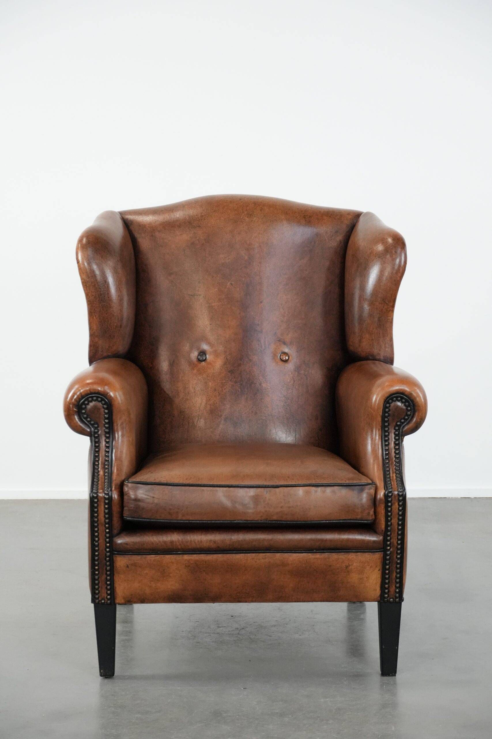 Sheepskin wingback armchair with decorative nails and black piping