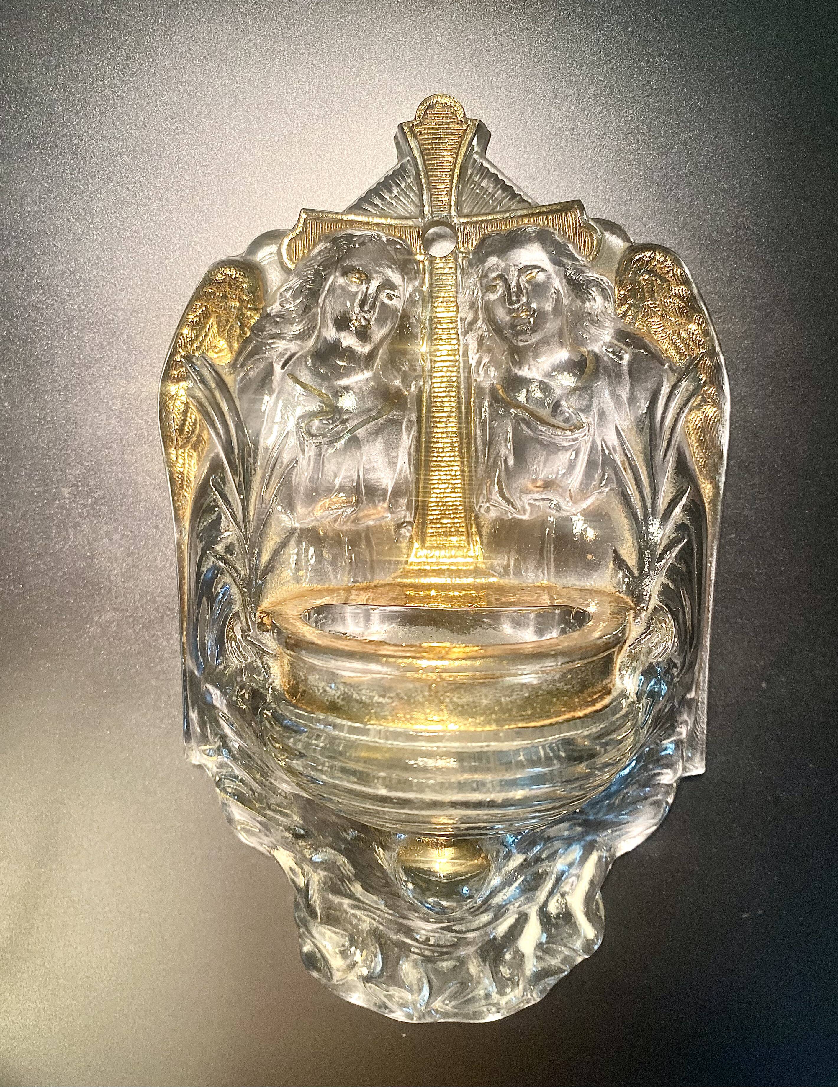 Old wall-mounted holy water font in moulded glass decorated with angels.