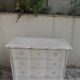 A beautifully crafted crossbow-shaped chest of drawers, finished in pearl grey with a whitewashed top.