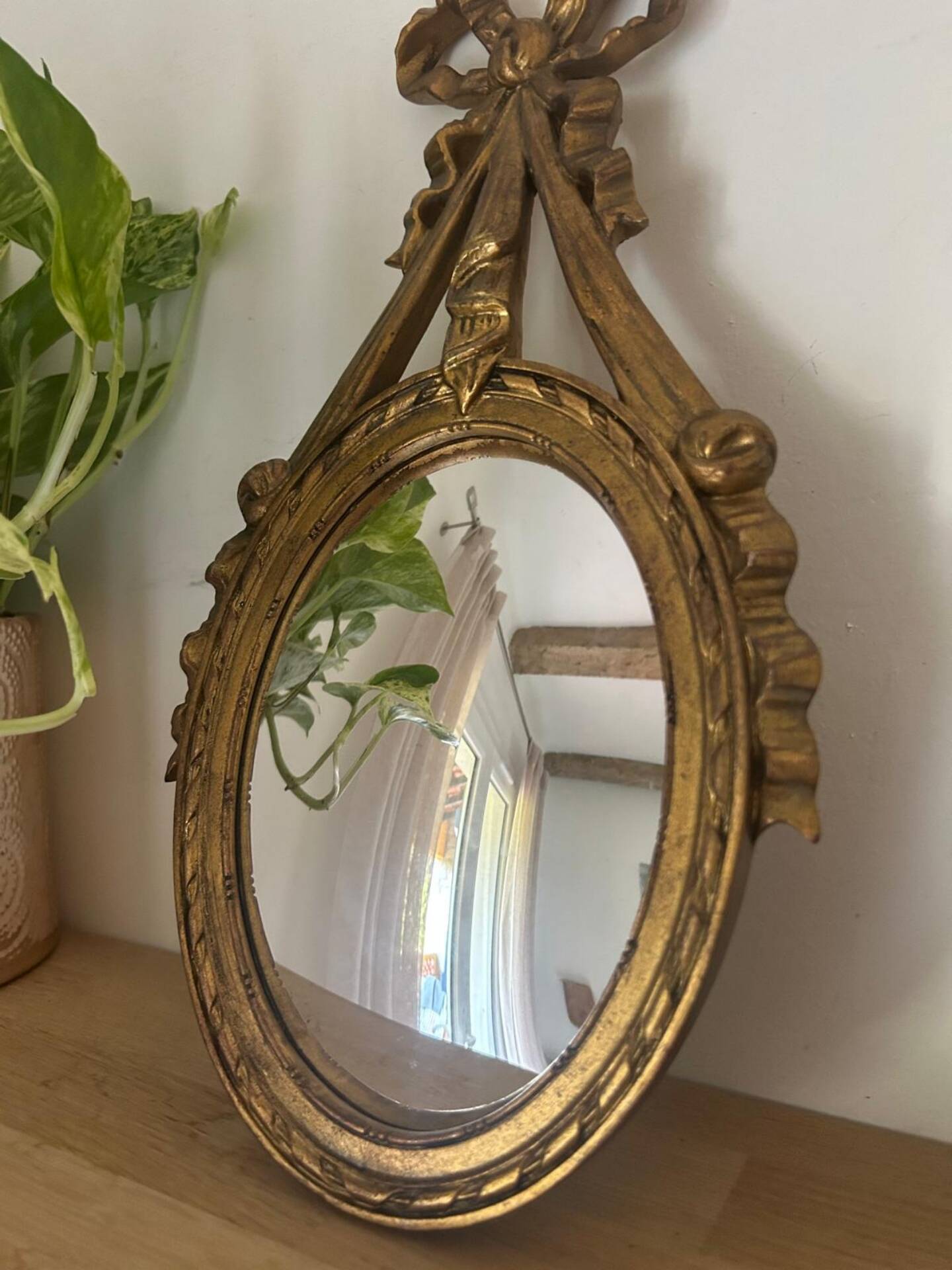 Oval convex witch mirror with golden ribbon mouldings.