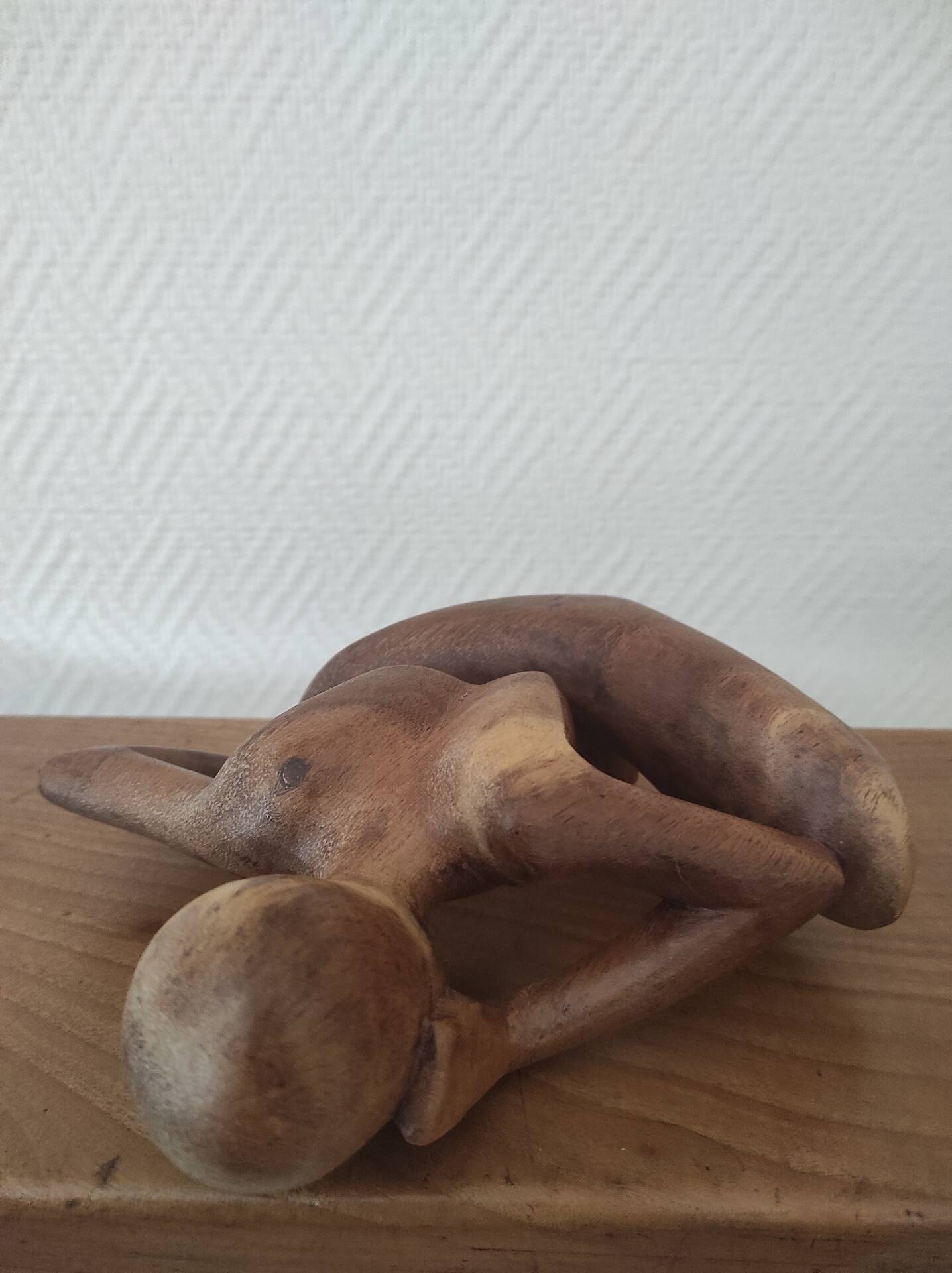 Wooden sculpted statuette of a woman in a pensive pose.