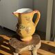 Large antique handmade ochre yellow jug with a pink flower pattern.