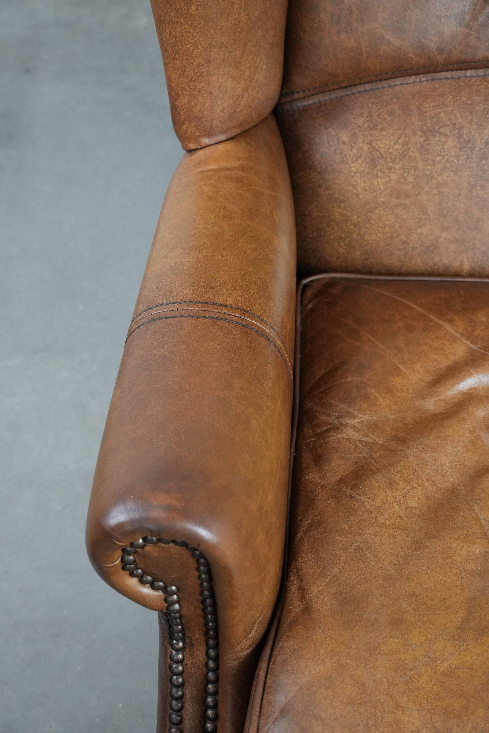 Fauteuil à oreilles de style anglais couleur cognac en cuir de vache.