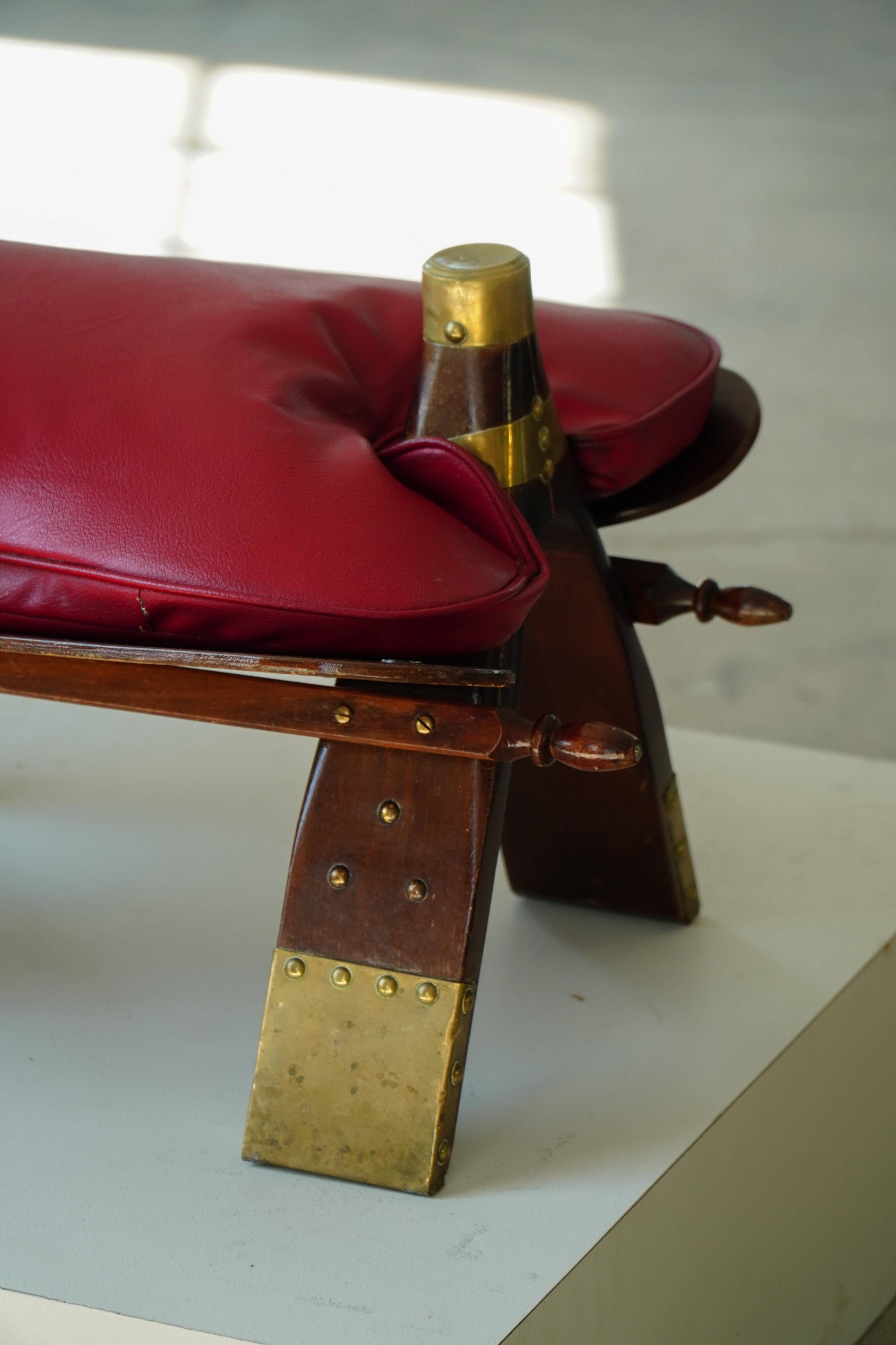 Moroccan stool in the shape of a camel saddle, stained wood, brass and leather, North Africa, 1980.