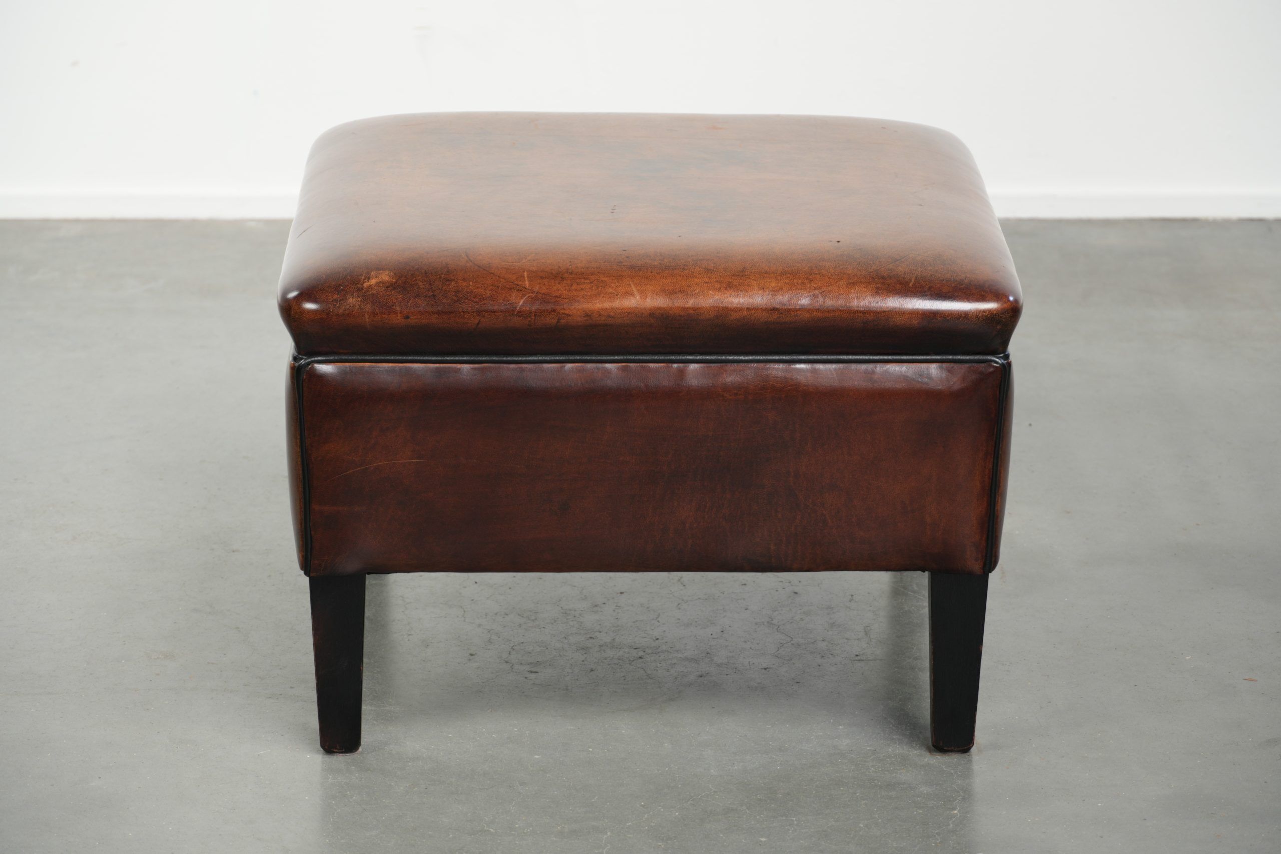 Large dark brown square ottoman made of sheepskin with black piping