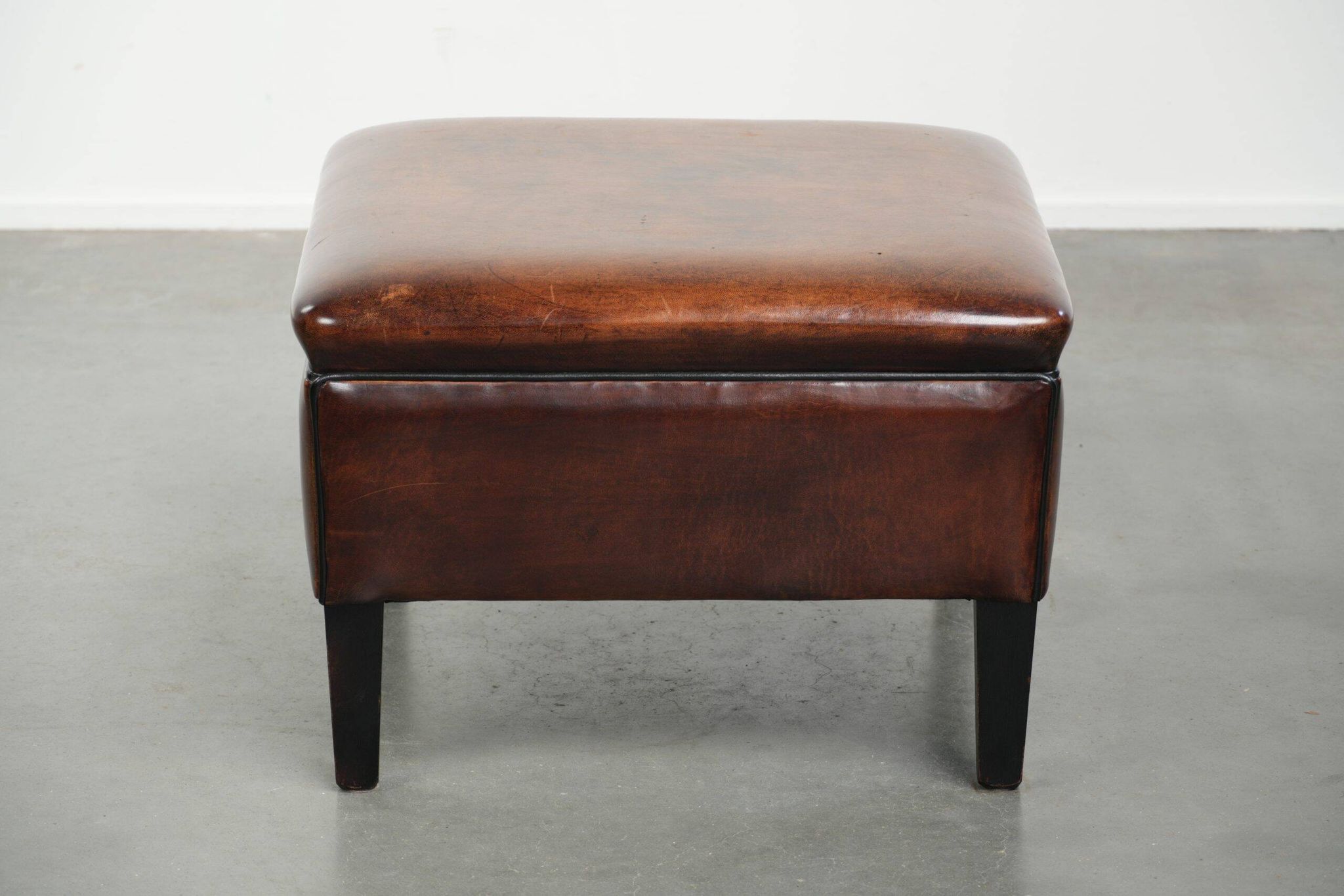 Pouf carré marron foncé en peau de mouton avec un passepoil noir.