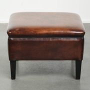Pouf carré marron foncé en peau de mouton avec un passepoil noir.