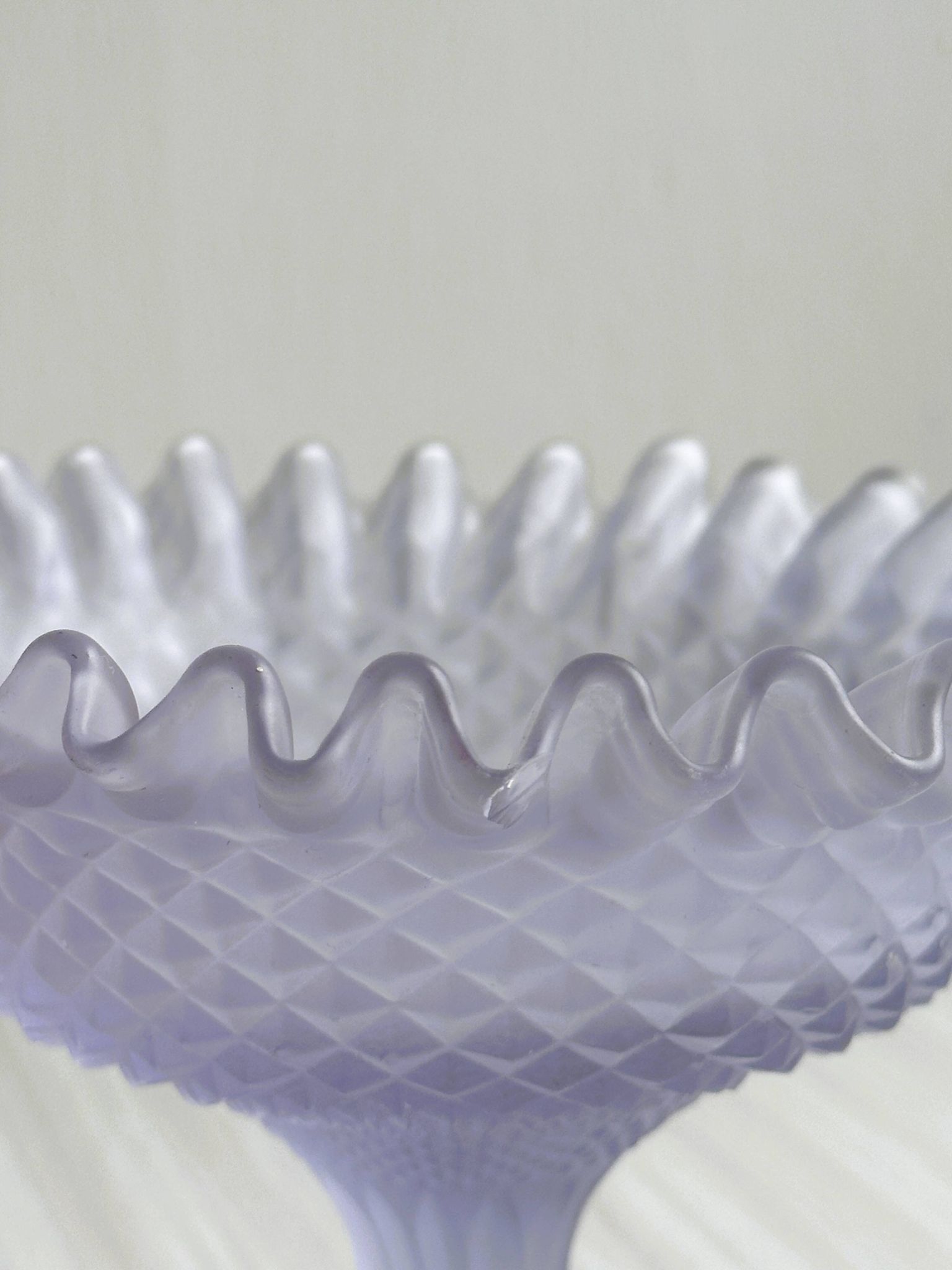 Purple glass pedestal bowl with wavy border and relief pattern.
