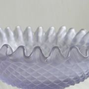 Purple glass pedestal bowl with wavy border and relief pattern.