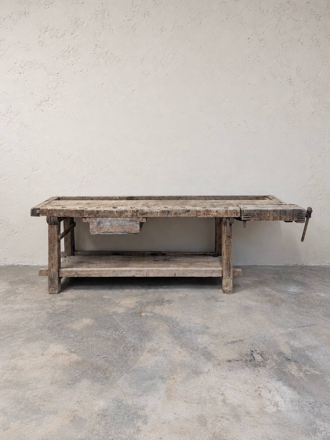 Antique wooden workbench with a vice and drawer.