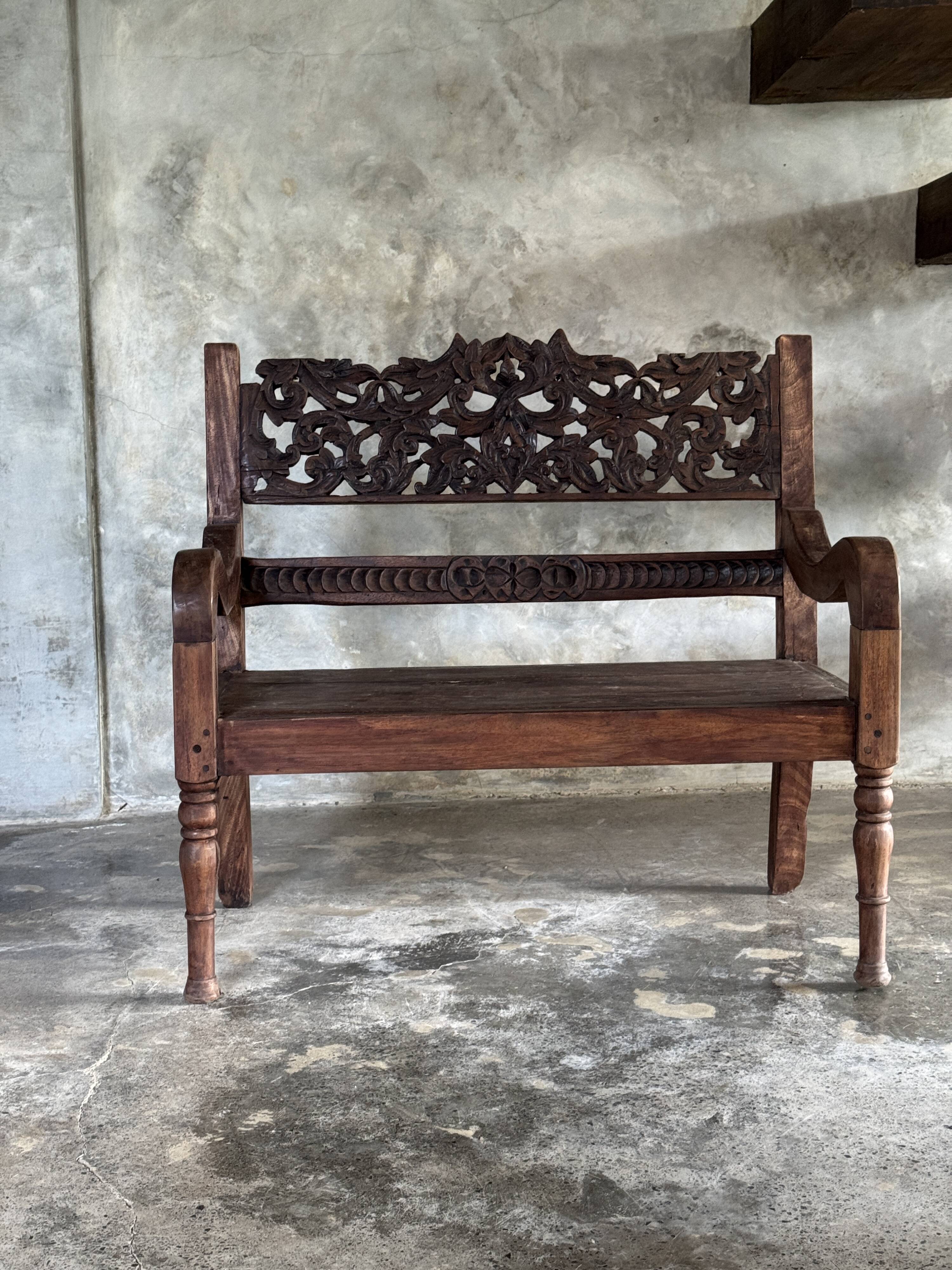 Small antique Indonesian bench in carved teak with plant and floral motifs.