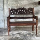 Small antique Indonesian bench in carved teak with plant and floral motifs.