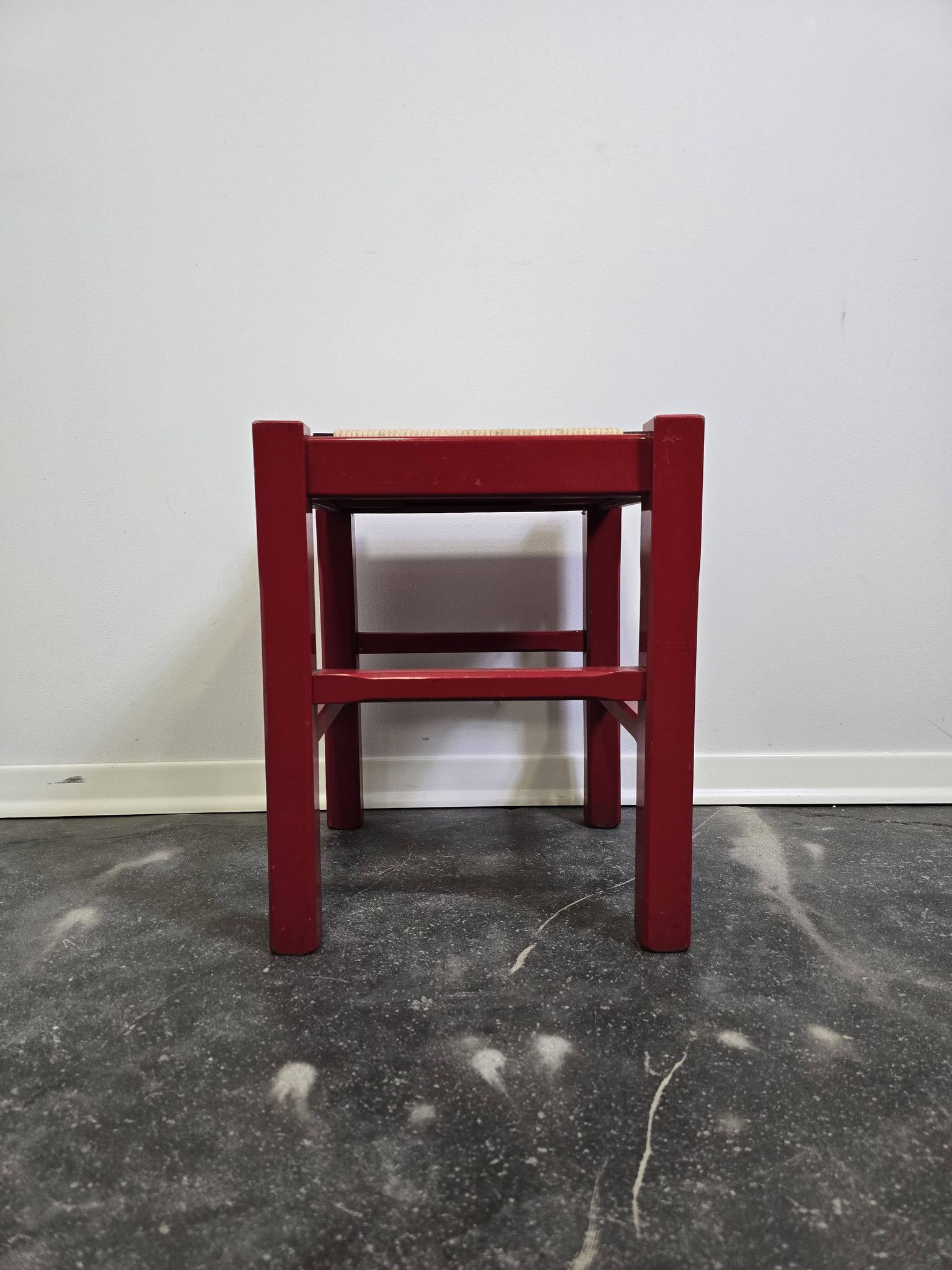Red wooden stool with a woven straw seat.