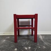 Red wooden stool with a woven straw seat.
