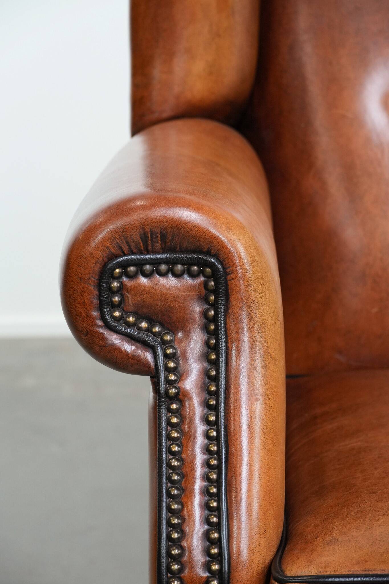 Large sheepskin wingback chair with black piping and decorative nails