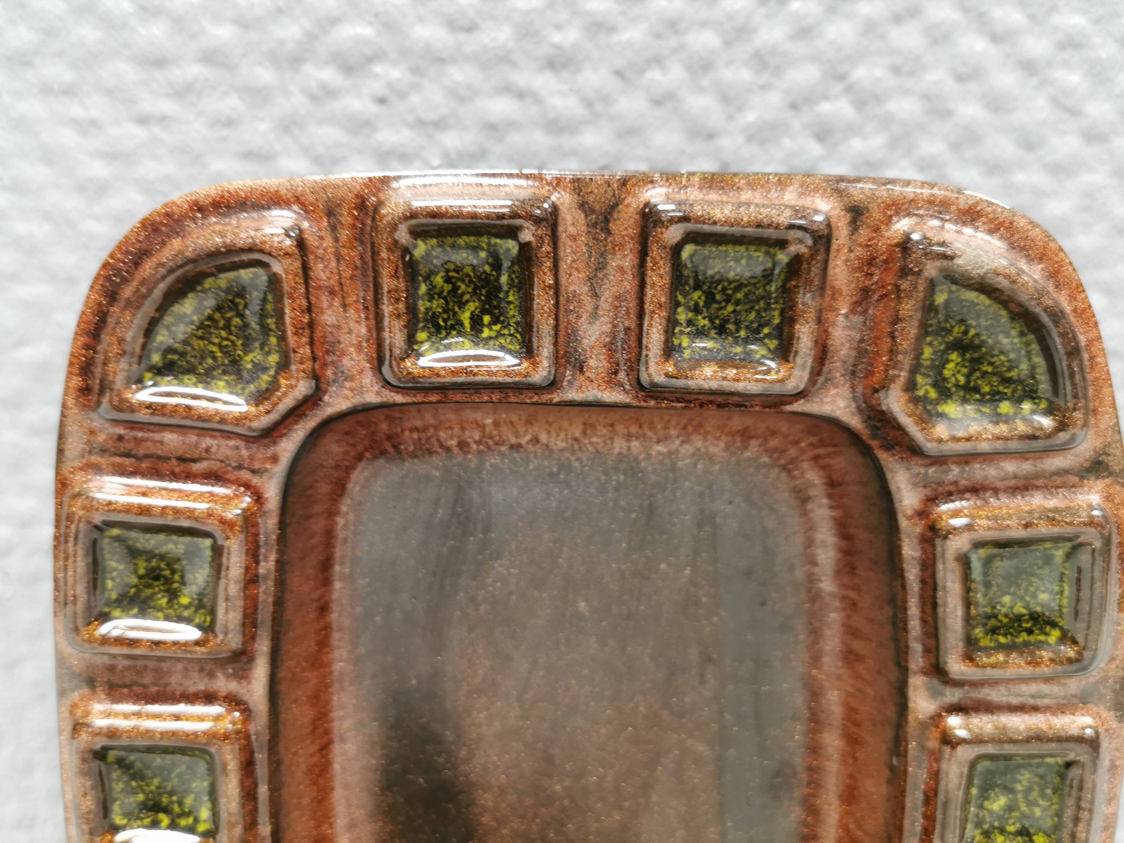 Wall-mounted candleholder in earthy, greenish, golden colours and shades.