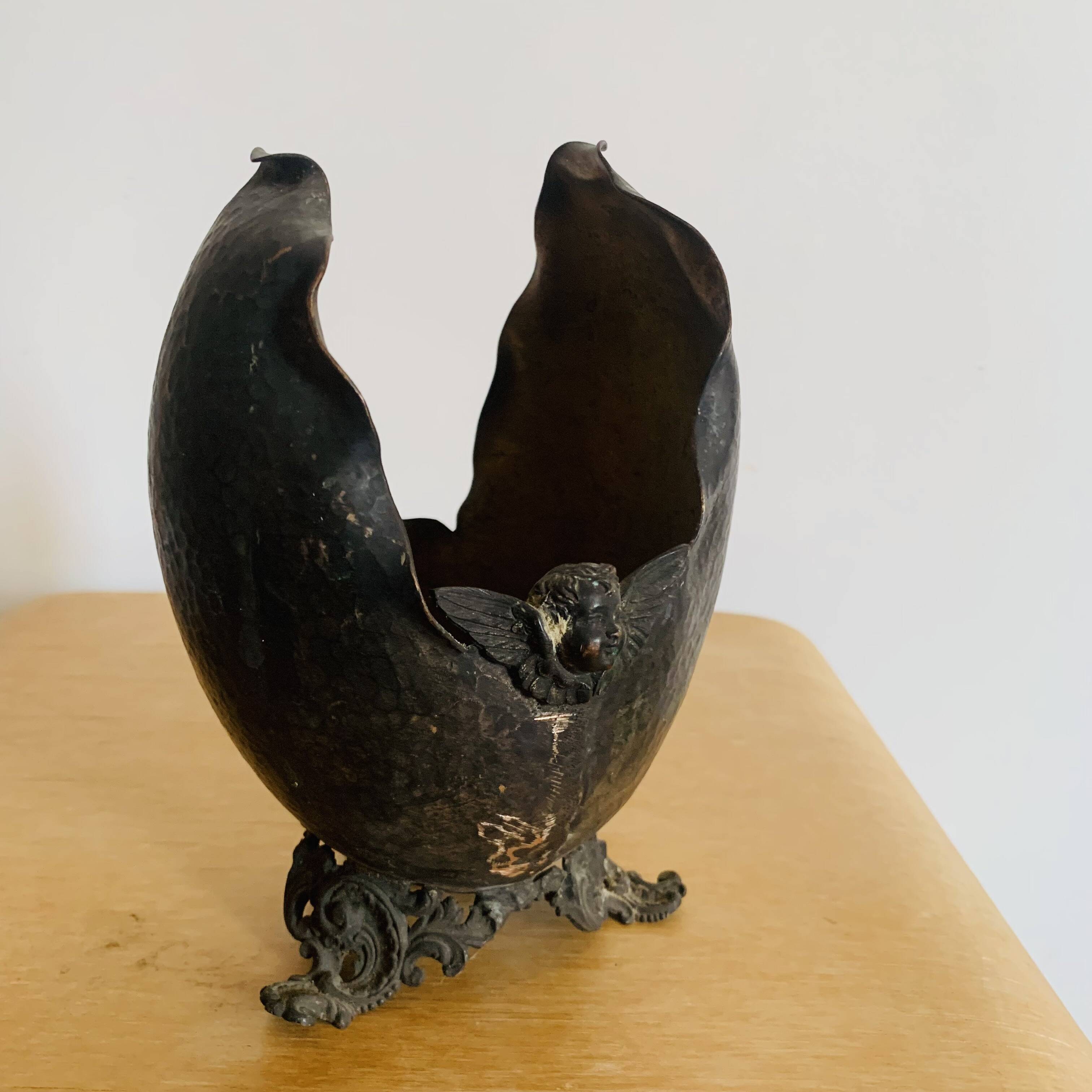 Antique decorative cup in hammered metal with putto design.