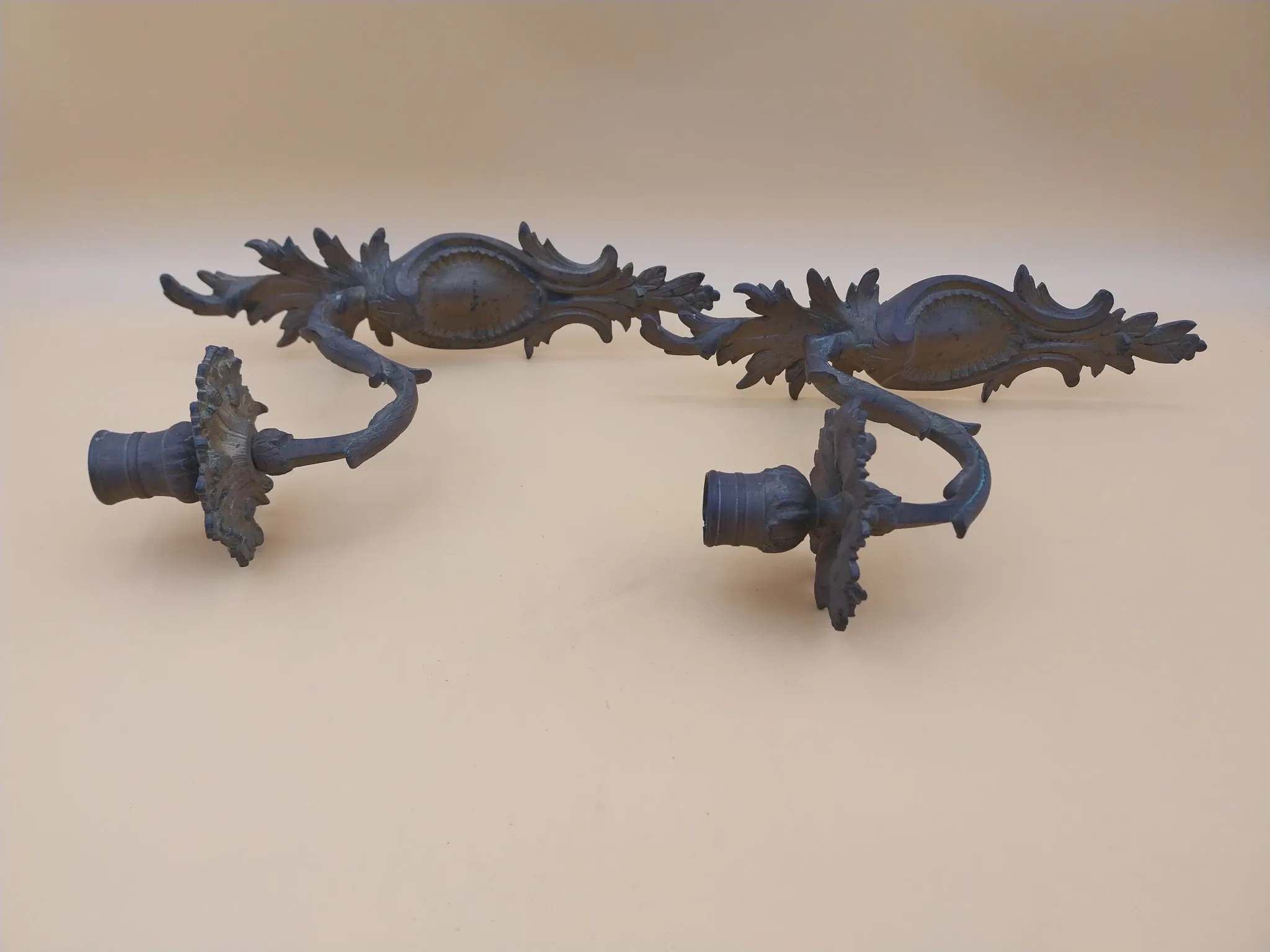 Pair of wall sconces in bronze candle holders with leaf medallion decoration.