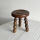 Small three-legged stool made of turned wood.