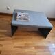 Minimalist/industrial coffee table with a black metal frame and a grey fabric top.