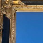 Miroir Baroque en bois doré sur fond noir.