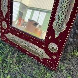 Large oriental mirror with embossed brass decoration on a red velvet background