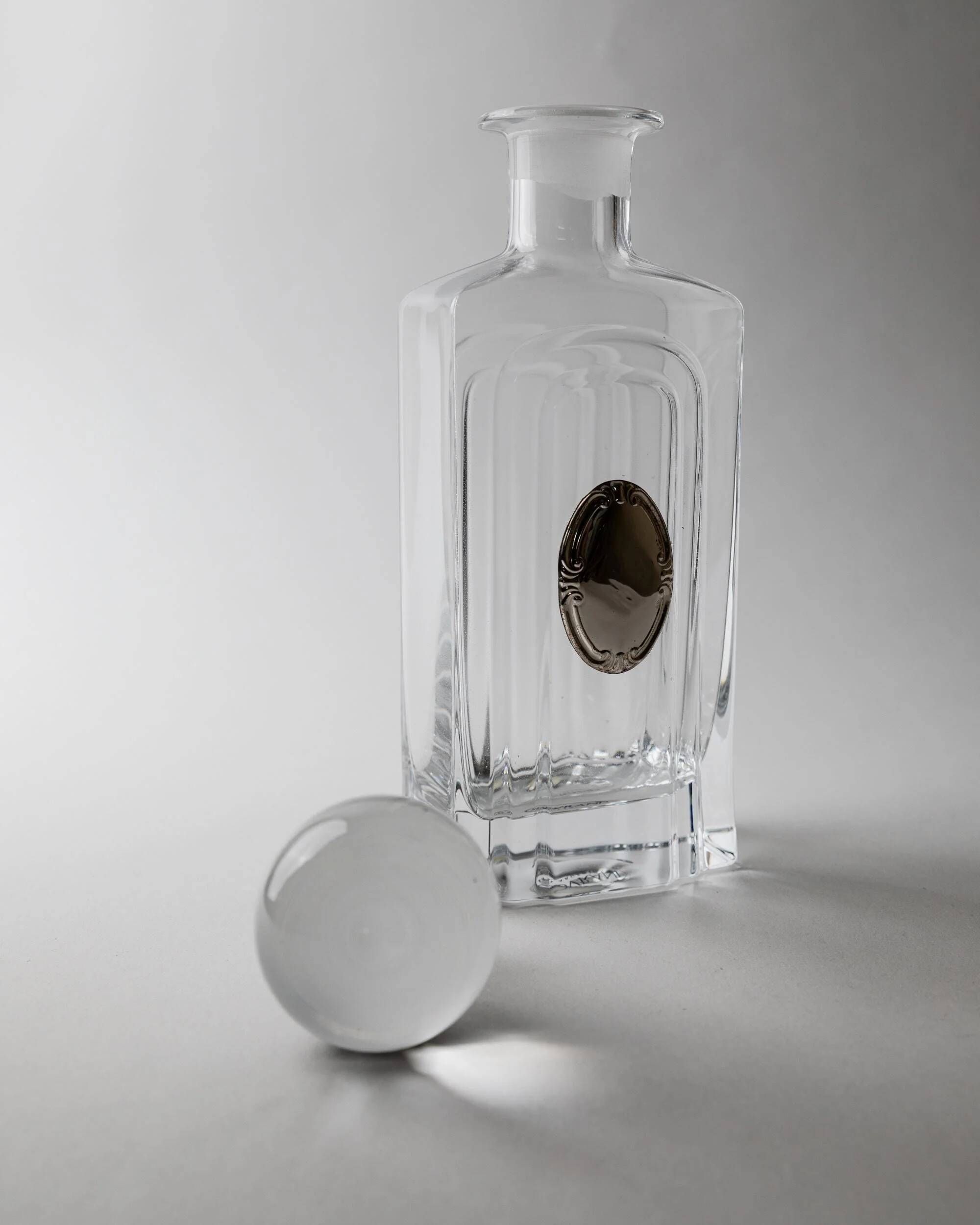 Vintage glass decanter from the 1980s, transparent glass with a silver plate and spherical stopper.